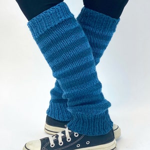 Puede incluir: Un par de polainas de punto azul turquesa con rayas blancas. Las polainas se llevan sobre unos leggings negros y unas zapatillas negras.