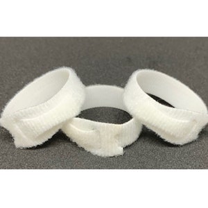 May include: Three white hook and loop cable ties, also known as  velcro straps, are shown in a close-up image. The ties are made of soft, flexible material and are designed to secure cables and wires.