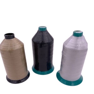 以下が含まれることがあります： ベージュ、黒、白の糸巻きが3つあります。各糸巻きは緑色の台座と黒い上部があります。