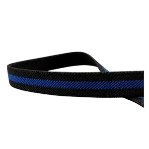 Puede incluir: Primer plano de una banda elástica a rayas negras y azules. La banda tiene una fina raya azul en el centro. El fondo es blanco liso.