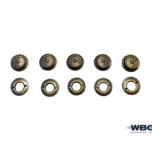 Pode incluir: Oito botões de metal de cor dourada antiga com um design decorativo. Os botões têm um centro elevado com um padrão floral e uma borda exterior lisa. Os botões estão dispostos em duas filas de quatro.