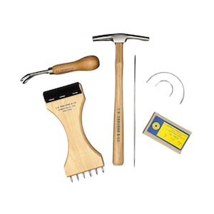 Puede incluir: Un conjunto de herramientas de marroquinería, que incluye un martillo, una lezna, un cepillo para rascar, agujas y un paquete de agujas. Las herramientas tienen mangos de madera y cabezas de metal. El martillo tiene una cabeza plana y un mango de madera.