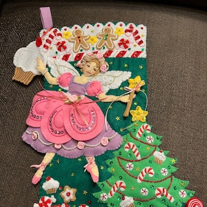 Könnte beinhalten: Handgefertigter Weihnachtsstrumpf mit grünem Hintergrund, der eine Ballerina-Fee in einem rosa Kleid und einen Weihnachtsbaum zeigt. Verziert mit Lebkuchenmännern, Zuckerstangen, Cupcakes und einem rosa Band. Die Oberseite hat einen weißen, gewellten Rand.