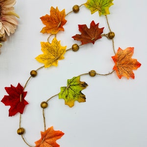 May include: A fall-themed garland with brown wooden beads and colourful maple leaves in shades of red, orange, yellow, and green.