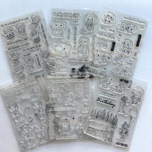 May include: Five clear silicone stamp sheets featuring various cartoon animal illustrations, including mice, rabbits, elephants, and bears, alongside birthday cakes, balloons, and text phrases like "you're the apple of my eye" and "world's best dad."