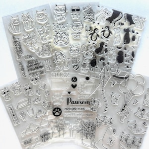 May include: A collection of clear silicone stamps featuring various cat illustrations, paw prints, balloons, kites, and text phrases like I love cats, Hugz, and you are Pawsom. The stamps are arranged on transparent sheets for crafting projects.