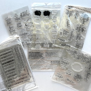 May include: A collection of five clear photopolymer stamp sets in plastic packaging. The sets feature various black printed sentiments, phrases, and decorative elements like grapes, vines, and speech bubbles for crafting and card making projects.