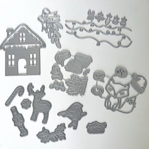 May include: A collection of silver-colored metal die cuts in various Christmas-themed shapes. Includes a house, reindeer, fox, ornaments, holly, and a candy cane. These are likely used for crafting and scrapbooking projects.