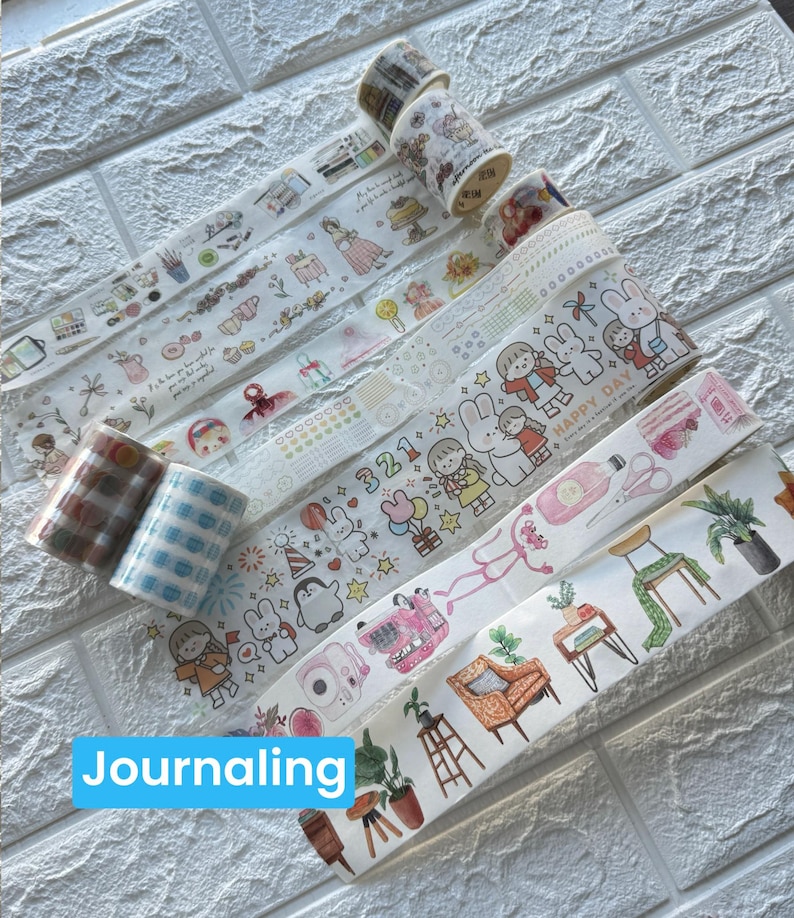 May include: A selection of decorative washi tapes featuring diverse designs such as floral motifs, cartoon characters, and geometric patterns. The tapes are presented in rolls and strips, ideal for journaling and craft activities. The word "Journaling" is in a blue box.
