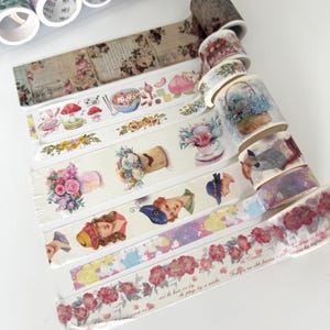 May include: A selection of decorative washi tapes with floral, vintage, and whimsical designs. The tapes display illustrations of flowers, hats, and other decorative elements. The colour palette includes soft pastels and earth tones, ideal for scrapbooking and crafting projects.
