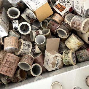 May include: A collection of decorative washi tape rolls with various vintage-inspired designs. The tape features images of botanical illustrations, architectural sketches, and handwritten text in shades of brown, beige, and green.