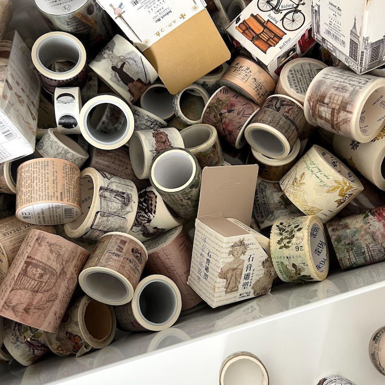 May include: A collection of decorative washi tape rolls with various vintage-inspired designs. The tape features images of botanical illustrations, architectural sketches, and handwritten text in shades of brown, beige, and green.