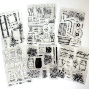 May include: Clear stamps with various garden and home-themed designs. Includes images of potted plants, watering cans, wheelbarrows, and text like "Happy Harvest Blessings" and "Simply Thankful". Also features cactus and photo frame designs.