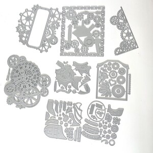 May include: A collection of gray metal die cuts in various steampunk-inspired designs. The shapes include gears, frames, a fish, and other mechanical elements. These die cuts are ideal for crafting and scrapbooking projects.