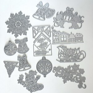 May include: A collection of silver-colored metal die cuts in various Christmas-themed shapes. The shapes include snowflakes, bells, ornaments, mice, a sleigh, a house, and a stocking. The die cuts are intricate and detailed, perfect for crafting projects.