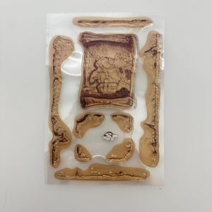 May include: Clear sheet of transparent stamps with a brown and white design. The stamps feature a scroll with a map inside, and several border designs.