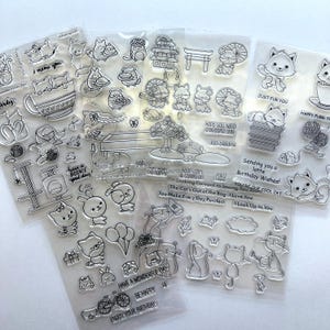 May include: A collection of clear photopolymer stamp sheets featuring various cartoon cat illustrations, including cats in teacups, on cat trees, and with yarn balls. The sets include phrases like "I meow you," "Just fur you," and "Happy purr-thday."