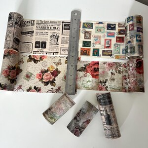 May include: Several rolls of decorative washi tape with vintage designs. The tape features floral patterns, newspaper clippings, postage stamps, and text like "Coffee Shop" and "Married Today." A metal ruler is placed next to the tape.