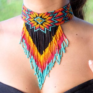 May include: A colourful beaded choker necklace with a geometric pattern and fringe. The necklace is made of turquoise, orange, yellow, red and black beads.