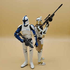 May include: Two Star Wars action figures, one in blue and white armour holding a blaster rifle, the other in tan and white armour holding a black rifle.
