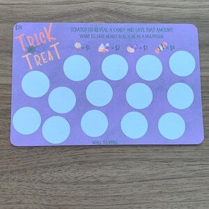May include: A purple and white Halloween-themed scratch-off game card with the words "Trick Treat" and "$35". The card has 12 circles that can be scratched to reveal a candy and save that amount. The card also includes a die that can be rolled as a multiplier. The card says "Scratch to reveal a candy and save that amount! Want to save more? Roll a die as a multiplier!"