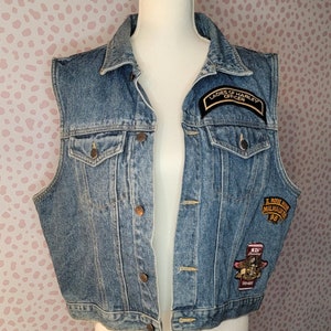 May include: A blue denim vest with multiple patches, including a "Ladies of Harley Officer" patch and a "I Rode My 1st Million Miles Milwaukee '98" patch.