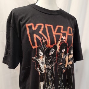 May include: Black t-shirt featuring a graphic of the band KISS in their iconic makeup. The band members are in a concert pose with the word "KISS" in red neon lights above them. The text "End of the Road World Tour" is printed below the band members.