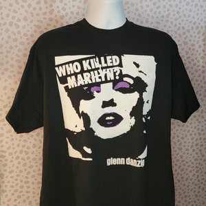 May include: Black t-shirt with a white graphic of Marilyn Monroe's face and the text "WHO KILLED MARILYN?" in purple. The text "Glenn Danzig" is printed below the graphic.