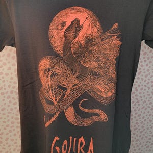 K&ouml;nnte beinhalten: Schwarzes T-Shirt mit einem orangefarbenen Aufdruck einer Schlange, die sich um einen Mond windet, mit dem Wort "GOJIRA" darunter.