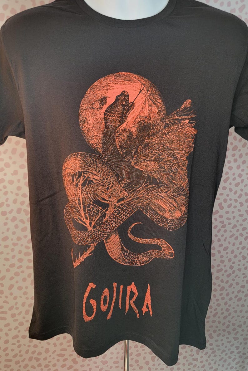K&ouml;nnte beinhalten: Schwarzes T-Shirt mit einem orangefarbenen Aufdruck einer Schlange, die sich um einen Mond windet, mit dem Wort "GOJIRA" darunter.