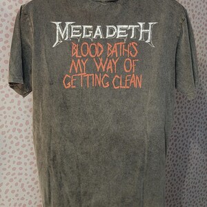 May include: A gray t-shirt featuring the band name "Megadeth" in white, with the text "Blood Baths My Way of Getting Clean" in orange. The shirt has a vintage, worn look.