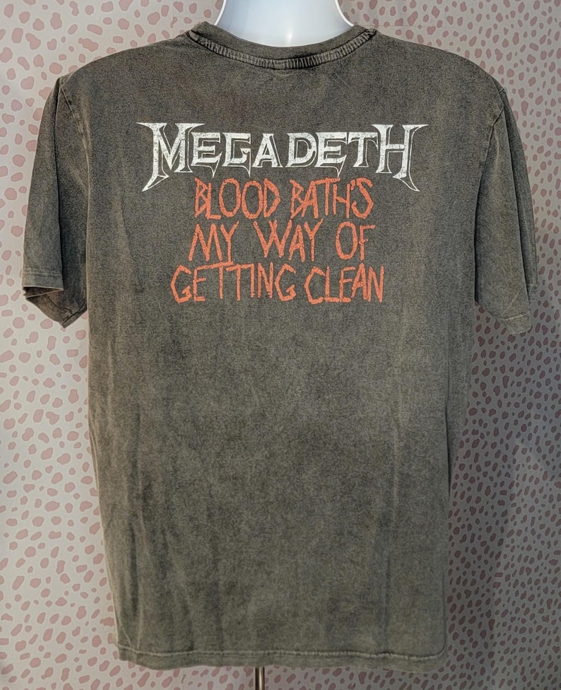 May include: A gray t-shirt featuring the band name "Megadeth" in white, with the text "Blood Baths My Way of Getting Clean" in orange. The shirt has a vintage, worn look.