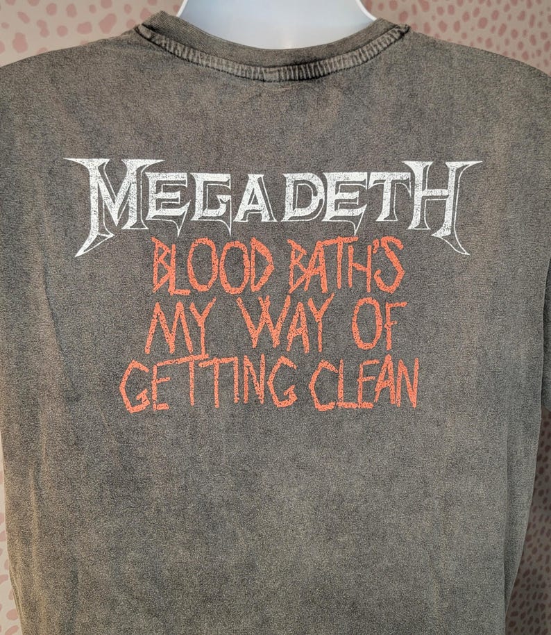 May include: Gray t-shirt with the band name "Megadeth" in white, stylized lettering. Below, in orange letters, the text reads "Blood Baths My Way of Getting Clean". The shirt has a vintage, washed appearance.