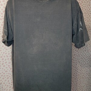 Peut inclure: Un t-shirt gris &agrave; manches courtes avec un col rond. Le t-shirt a un aspect d&eacute;lav&eacute; et l&eacute;g&egrave;rement vieilli. Les manches sont retrouss&eacute;es. Le t-shirt est pr&eacute;sent&eacute; sur un mannequin blanc.