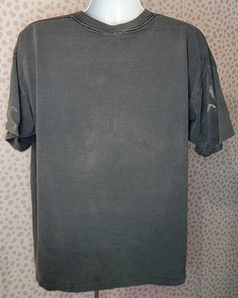 Peut inclure: Un t-shirt gris &agrave; manches courtes avec un col rond. Le t-shirt a un aspect d&eacute;lav&eacute; et l&eacute;g&egrave;rement vieilli. Les manches sont retrouss&eacute;es. Le t-shirt est pr&eacute;sent&eacute; sur un mannequin blanc.