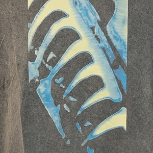 May include: A gray t-shirt featuring the band name "nine inch nails" in white block letters. The shirt has a graphic design of a blue and yellow skeletal structure. The design is centered on the shirt.