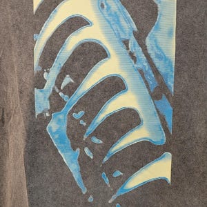 May include: Dark gray t-shirt featuring the band name "nine inch nails" in yellow block letters. The shirt has a graphic design in blue and yellow, with a faded, vintage look.