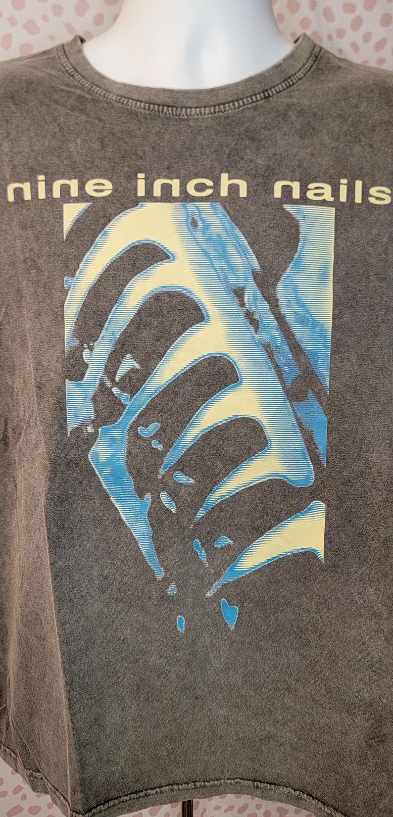 May include: Dark gray t-shirt featuring the band name "nine inch nails" in yellow block letters. The shirt has a graphic design in blue and yellow, with a faded, vintage look.