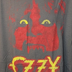 May include: Gray t-shirt featuring a red and yellow graphic of a face and the name "Ozzy Osbourne." The graphic has a distressed look. The shirt is displayed on a mannequin.
