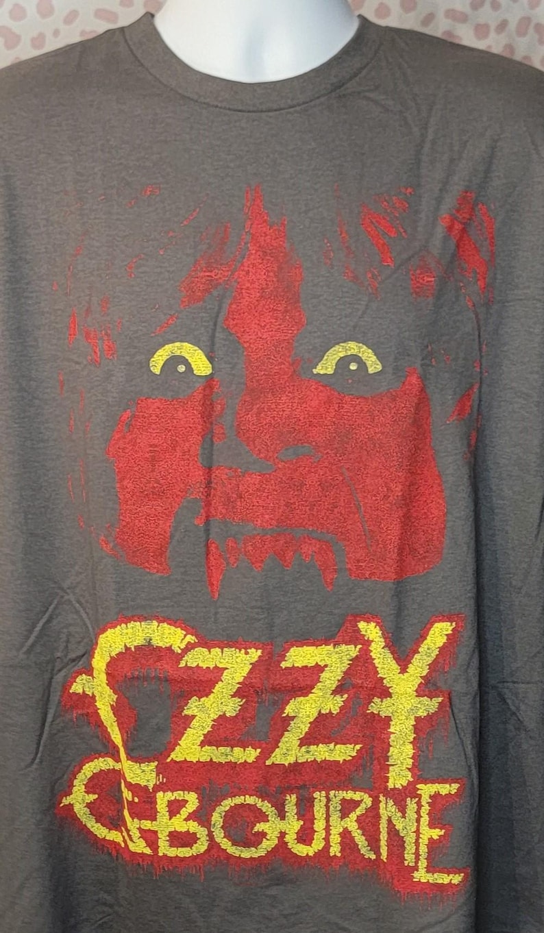 May include: Gray t-shirt featuring a red and yellow graphic of a face and the name "Ozzy Osbourne." The graphic has a distressed look. The shirt is displayed on a mannequin.