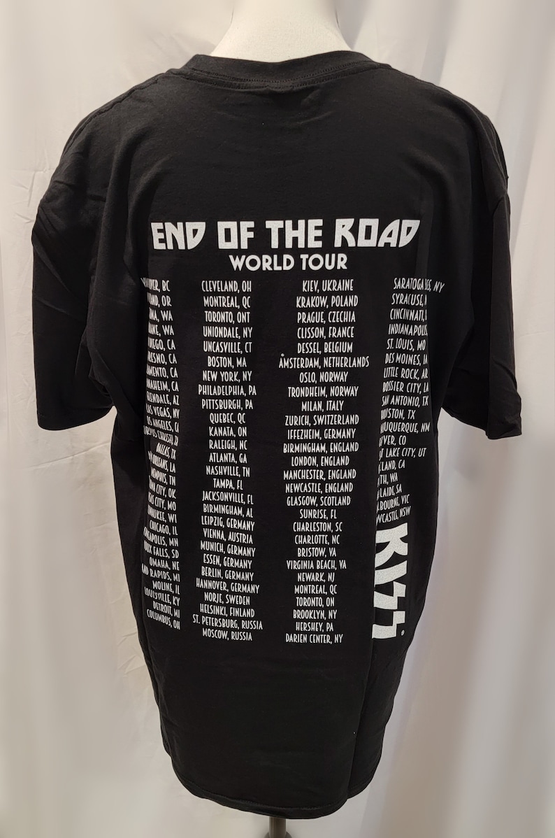May include: Black t-shirt with white text listing the cities on the "End of the Road World Tour" for the band KISS. The tour dates include cities in North America, Europe, and Russia.