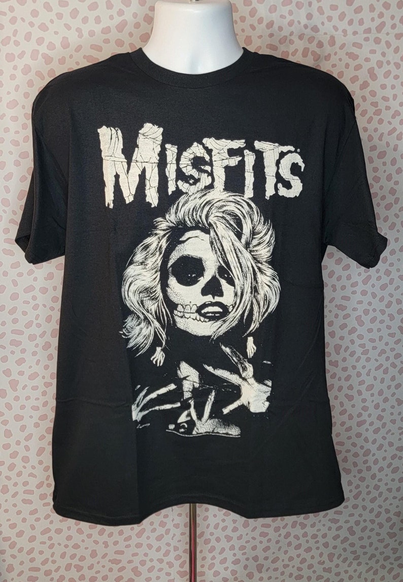 May include: Black t-shirt with a white graphic of a woman with a skull face and the word "Misfits" printed above her.