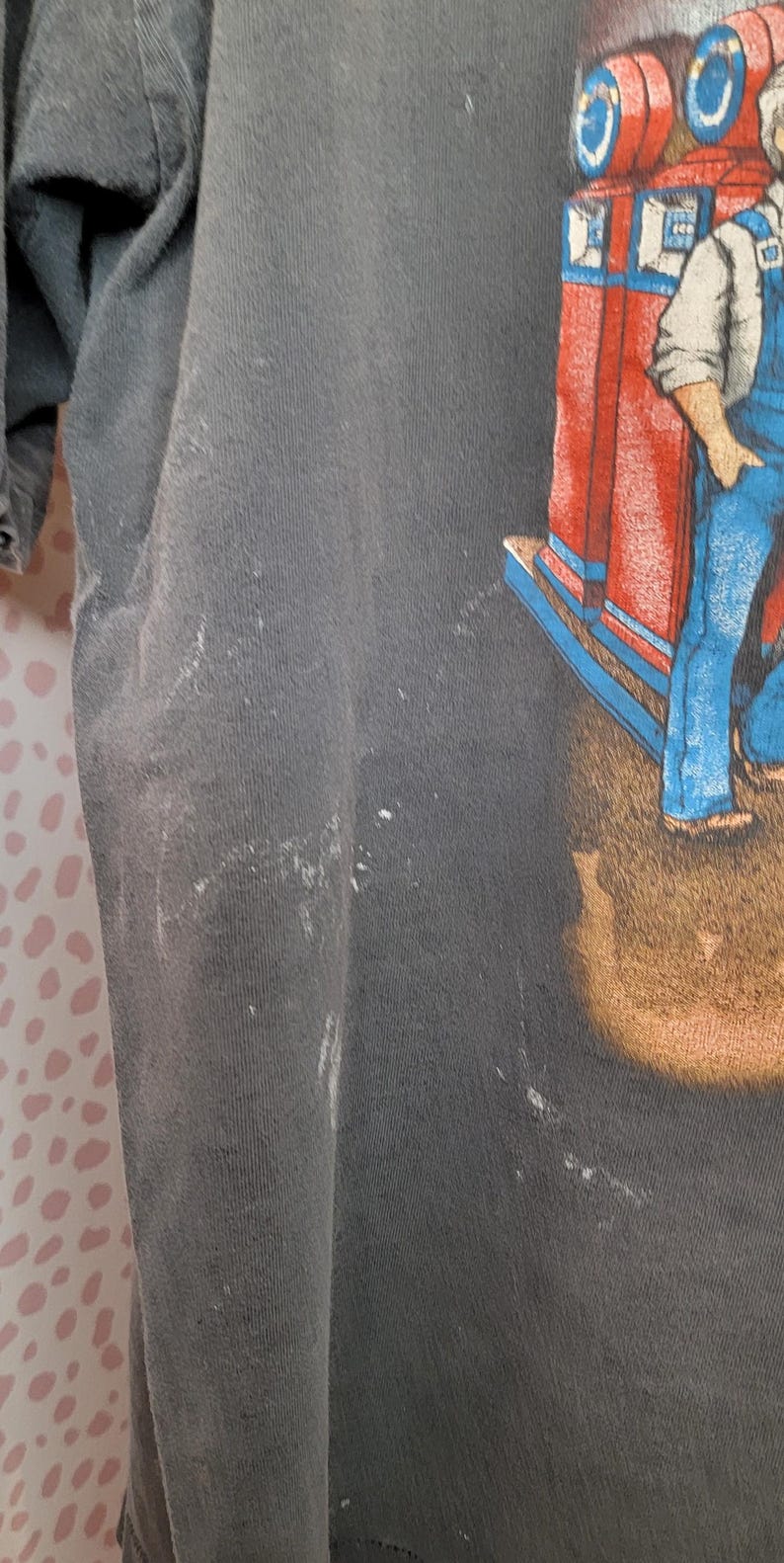 Peut inclure: T-shirt gris fonc&eacute; avec un graphisme color&eacute; d'un homme en salopette bleue et d'une structure rouge et bleue. Le t-shirt a un aspect us&eacute; avec quelques marques blanches.