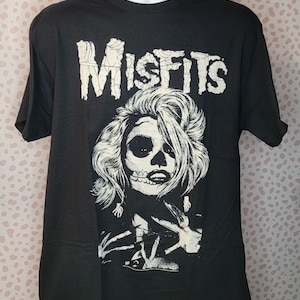 May include: Black t-shirt with a white graphic of a woman with a skull face and the word "MISFITS" above her.