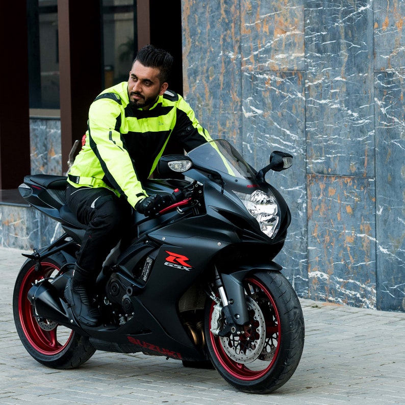 K&ouml;nnte beinhalten: Eine Person in einer leuchtend gelben und schwarzen Motorradjacke f&auml;hrt ein schwarzes Motorrad mit roten Akzenten. Das Motorrad hat eine schwarze Windschutzscheibe und einen schwarzen Sitz.