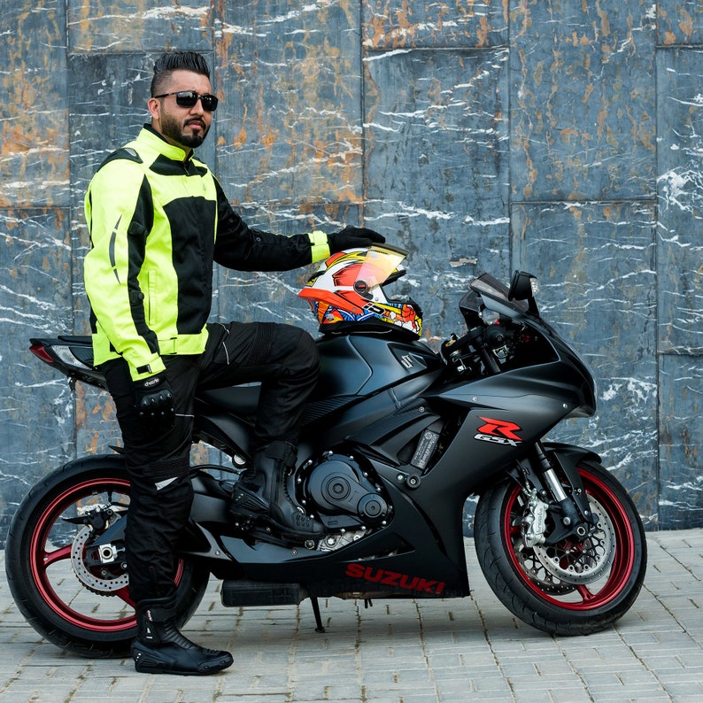 K&ouml;nnte beinhalten: Eine Person in einer gelben und schwarzen Motorradjacke sitzt auf einem schwarzen Suzuki Motorrad mit einem roten und gelben Helm auf dem Soziussitz.