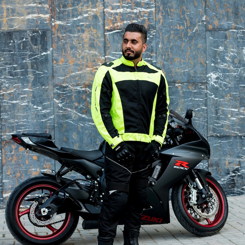 K&ouml;nnte beinhalten: Ein Mann in einer schwarzen und neongelben Motorradjacke steht neben einem schwarzen Motorrad. Das Motorrad hat ein rotes "R"-Logo an der Seite.