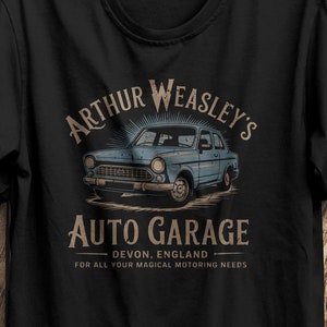 May include: Black t-shirt with a vintage-style graphic of a blue car and the text "Arthur Weasley's Auto Garage - Devon, England - For all your magical motoring needs."