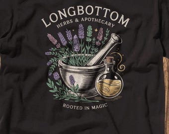 May include: Black t-shirt with a graphic of a mortar and pestle with lavender flowers and a bottle of potion. The text "Longbottom Herbs & Apothecary" and "Rooted in Magic" are printed on the shirt.