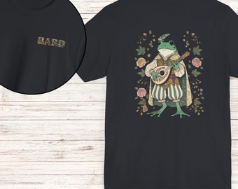 Puede incluir: Camiseta negra con una rana verde tocando un laúd en un entorno floral. La rana lleva un sombrero y un atuendo verde y blanco. El texto "BARD" está en la parte delantera de la camiseta.